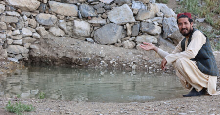 Faridullah sitter vid en reservoar och låter vatten strila mellan händerna.