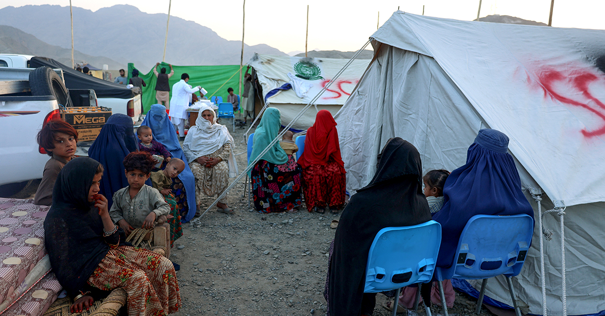 Kvinnor och barn sitter utanför ett av SAKs tält i flyktinglägret.