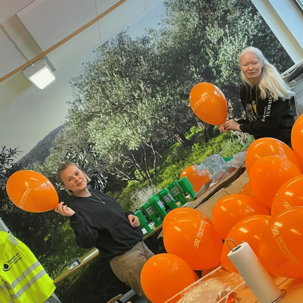 Två personer håller i varsin orange ballong. På bordet framför dem syns flera uppblåsta orangea ballonger