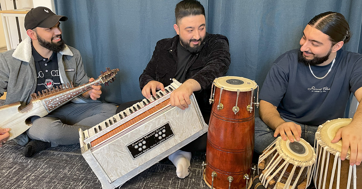De tre musikerna sitter på golvet, spelar sina instrument och ser leende på varandra.