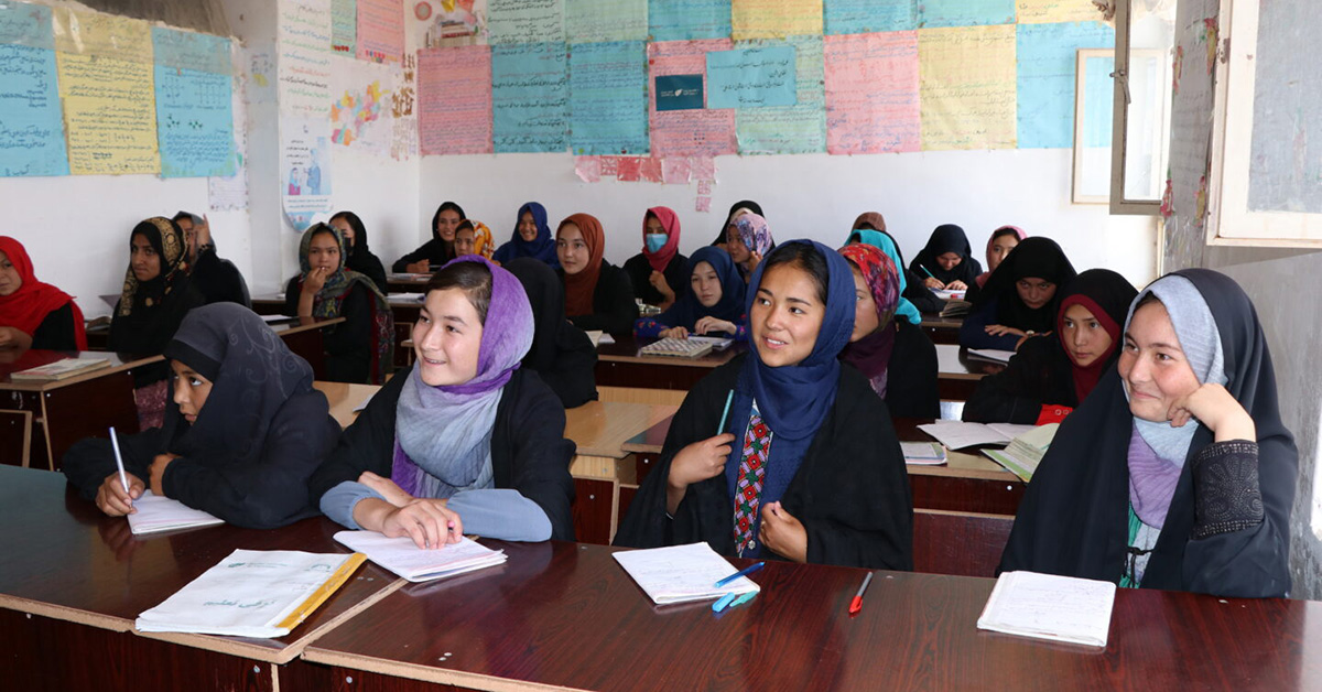 Unga kvinnor i ett afghanskt klassrum med färgglada planscher på väggarna.