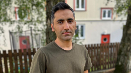 Man i halvfigur framför hus och träd.