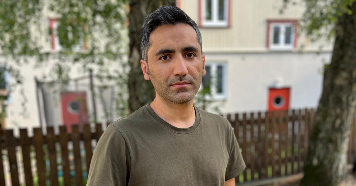 Man i halvfigur framför hus och träd.