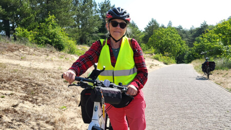Kvinna i cykelhjälm och cykelväst mellan sandbankar, med cykel.