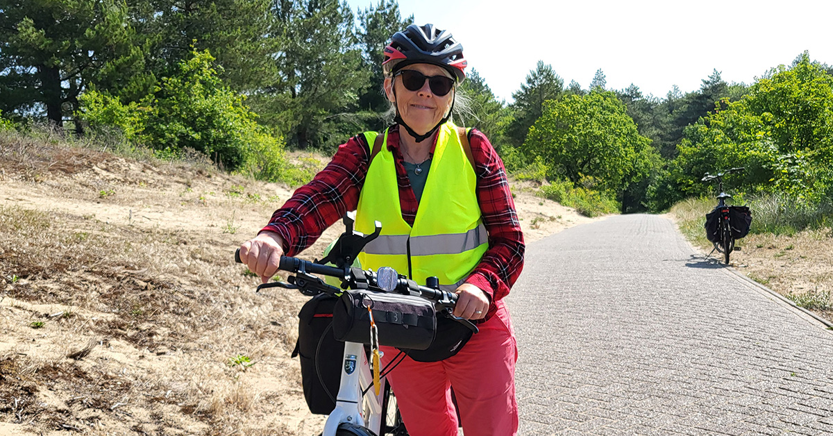 Kvinna i cykelhjälm och cykelväst mellan sandbankar, med cykel.