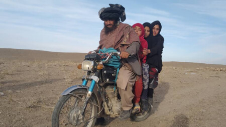 En man skjutsar sina tre döttrar på motorcykel i ett kargt afghanskt landskap.