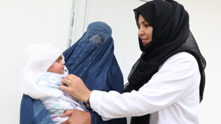 En barnmorska. till höger. undersöker en bebis som hålls av en kvinna i burka.