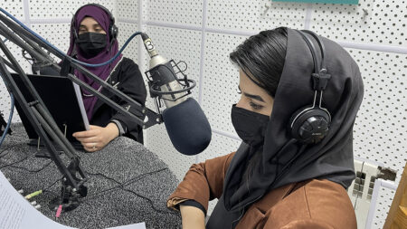 Två kvinnor med sjal och munskydd i en radiostudio.