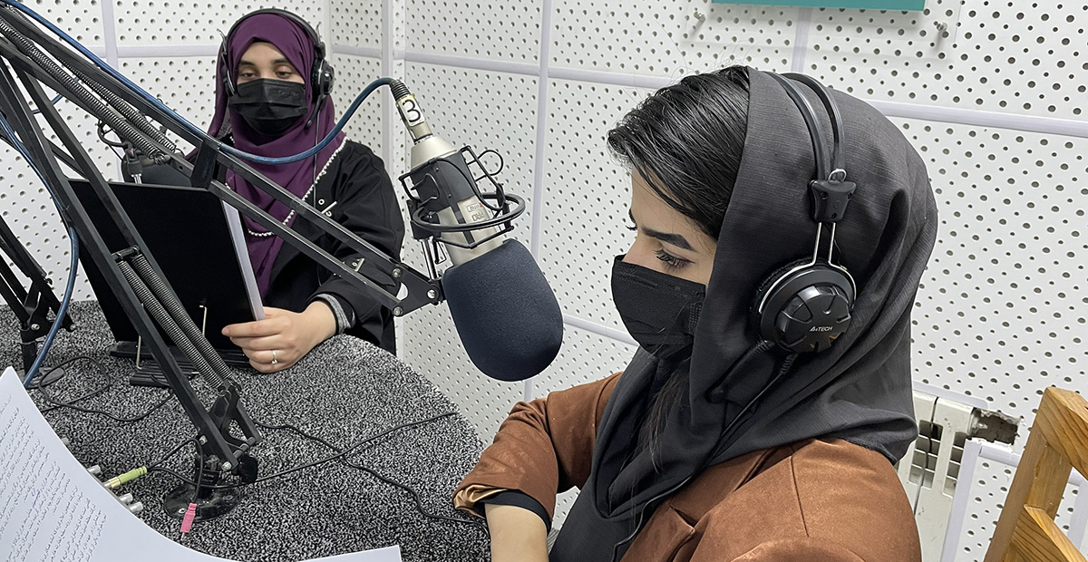 Två kvinnor med sjal och munskydd i en radiostudio.