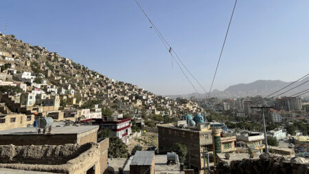Stadsvy över Kabul, gytter av hus med bergen och en blå himmel i bakgrunden.