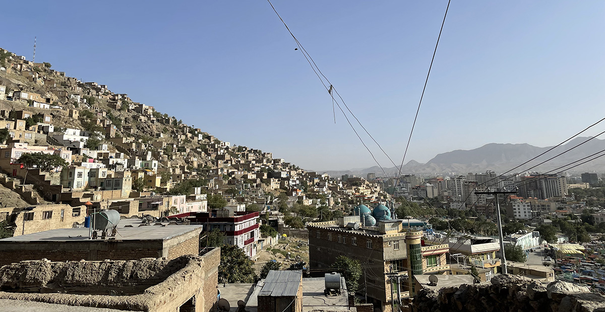 Stadsvy över Kabul, gytter av hus med bergen och en blå himmel i bakgrunden.