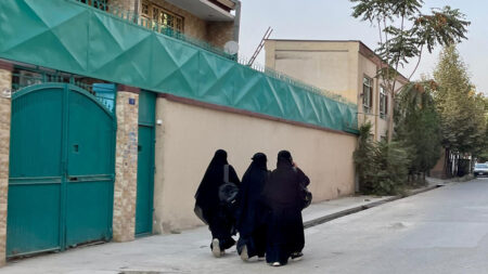 Tre unga afghanska kvinnor i täckande kläder syns bakifrån på en gata i Kabul.