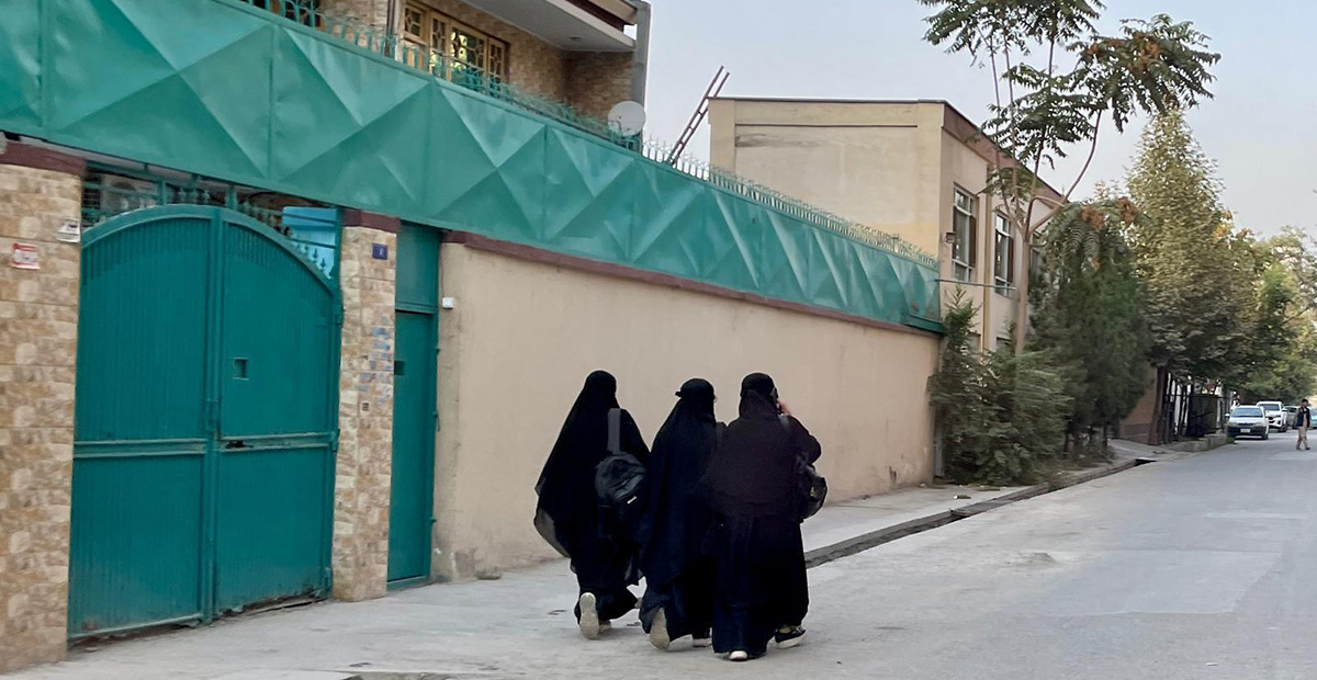 Tre unga afghanska kvinnor i täckande kläder syns bakifrån på en gata i Kabul.